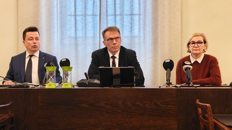 Three people sit at a table with a microphone in front of them.