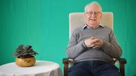 Allan Blom sitter i en fåtölj framför ett grönt tyg.