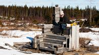 Pipopäinen mies istuu seinättömässä huussissa kevättalvella.