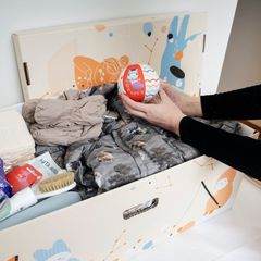 A woman is holding a small soft ball, over a baby box/ maternity package.