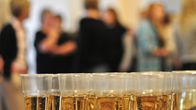 Rows of glasses filled with sparkling wine, with a blurry image of people in the background.