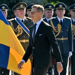 President Alexander Stubb walking in front of soldiers with a Ukrainian flag in the background.