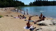 Folk solbadar och simmar vid en simstrand en solig sommardag.
