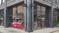 Katutasossa sijaitsevan liiketilan ikkunoista näkyy sisälle liikkeeseen. Ikkunateippauksessa lukee "The Laku" Sekä Kouvolan lakritsi Helsinki. 