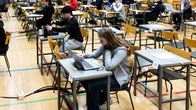 Unga sitter vid små bort i rader och skriver studentprov.