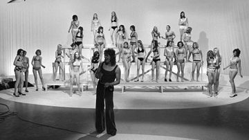 Markku Aro esiintyy 1972. Taustalla bikinipukeisia naisia.
