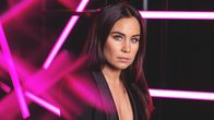 Ruskeahiuksinen laulaja Abreu katsoo vakavana kameraan pää kallellaan, etualalla ja taustalla neonpinkkejä valoelementtejä. Päällä mustat vaatteet