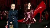 Meryl Streep ja Anne Hathaway poseeraavat valtavan kokoisen korkokengän vieressä.