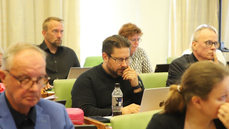 Mustaan pukeutunut, lyhyttukkainen ja silmälasipäinen valtuutettu istuu pöydän takana Porin kaupungintalon salissa muiden valtuutettujen keskellä. 
