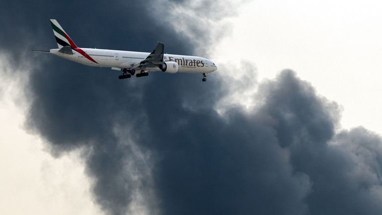 Emirates-lentokone laskeutuu, taustalla musta pilvi.
