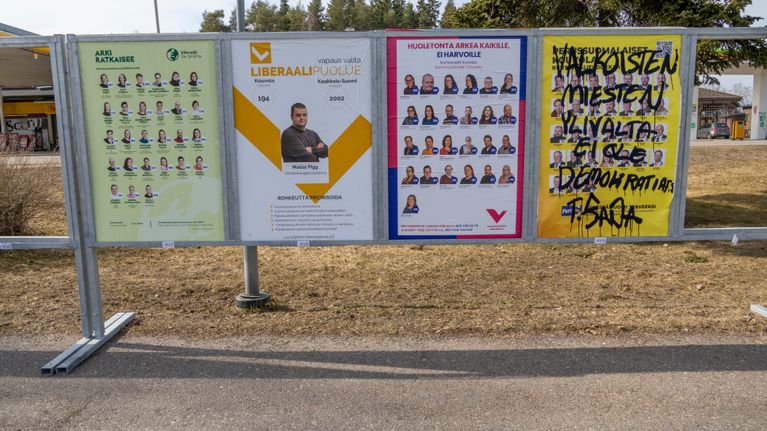 Vaalijulistetelineessä neljän puolueen julisteet. Ainoastan perussuomalaisten julistetta on töhritty mustalla tekstillä.