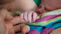 Vastasyntynyt värikkääseen pyyhkeeseen kääritty vauva pitää ryppyisillä sormillaan kiinni isänsä etusormesta.