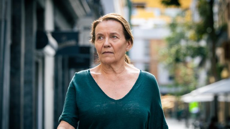 Rikostutkija Hilkka Mäntymäki (Riitta Havukainen) kävelee kadulla yllään vihreä t-paita. Taustalla näkyy rakennuksia ja puita.