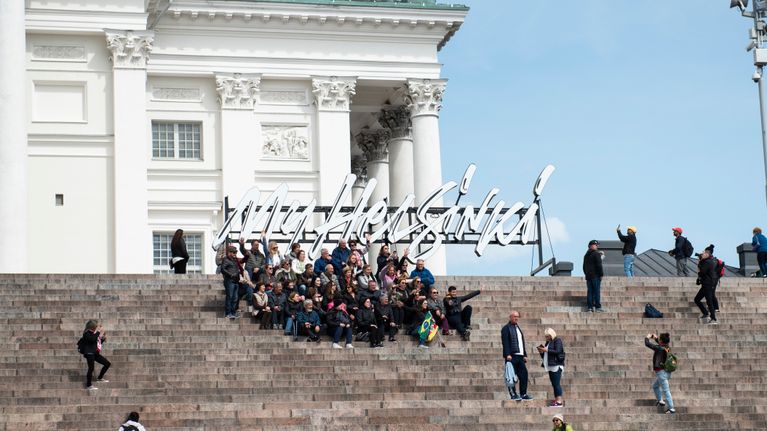 Turistit ottavat yhteiskuvaa Helsingin tuomiokirkon portailla.