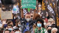 En ung tysk i flanellskjorta och rödfärgat snaggat hår sitter på sin kompis axlar i ett folkhav under en klimatdemonstration i Berlin. Ungdomen håller uppe en grön skylt med texten "Smells like air pollution". 