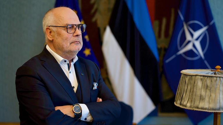 Silmälasipäinen harmaantunut mies puvussa seisoo Viron presidentinlinnan neuvotteluhuoneessa ja katsoo ulos, taustalla EU:n, Viron ja Naton liput.