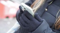 Teini-ikäinen tyttö hanskat ja takki päällä käyttää puhelinta ulkona