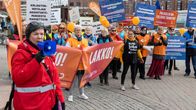 Ihmisiä kokoontuneena mielenosoitukseen. Kyltti "Lakko". Punaiseen takkiin pukeutunut Helena Nieminen puhuu megafoniin. 