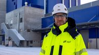 Teollisuusrakennuksen edustalla seisoo mies huomiotakissa ja valkoisessa kypärässä.