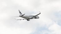 White Finnair jet in the sky with clouds in the background.