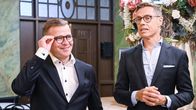 Petteri Orpo kohentaa silmälasejaan ja hymyilee rennon näköisenä. Alexander Stubb puhuu. Molemmilla puvut päällä, ei kravattia.