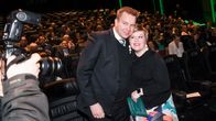 A man and a woman, both wearing dark jackets, pose for photographers arms around each other's shoulders, with conference delegates seated in the background.