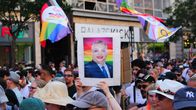 Ihmisiä Pridekulkueessa. Keskellä kyltti ja taustalla Pride-lippuja.