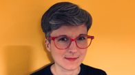Anna Mattilla seisoo keltaista taustaa vasten.