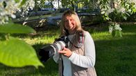 En person med kamera står på en gräsmatta under blommande träd.