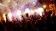 Rock-yhtye esiintyy lavalla, edessä yleisöä nauttii musiikista kädet ilmassa