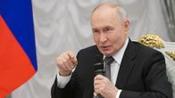 Vladimir Putin pitää mikrofonia kädessään puhuessaan pöydän ääressä.