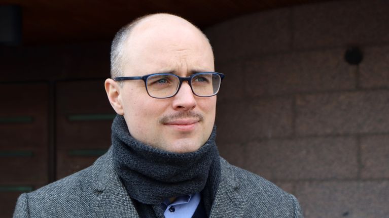 En man i glasögon och halsduk tittar snett mot höger.