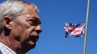 Nigel Farage kuvattuna sivusta sinistä taivasta vasten, taustalla liehuu Yhdistyneen kuningaskunnan lippu puolitangossa.