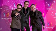 Axel Åhman, Kevin Holmström, och Jakob Norrgård poserar på röda mattan vid Melodifestivalen 2023. De är klädda i stiliga kostymer och står framför en bakgrund med festivalens logotyp.