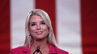 Leende kvinna med långt blont hår, med USA-flaggans röda ränder som bakgrund. 