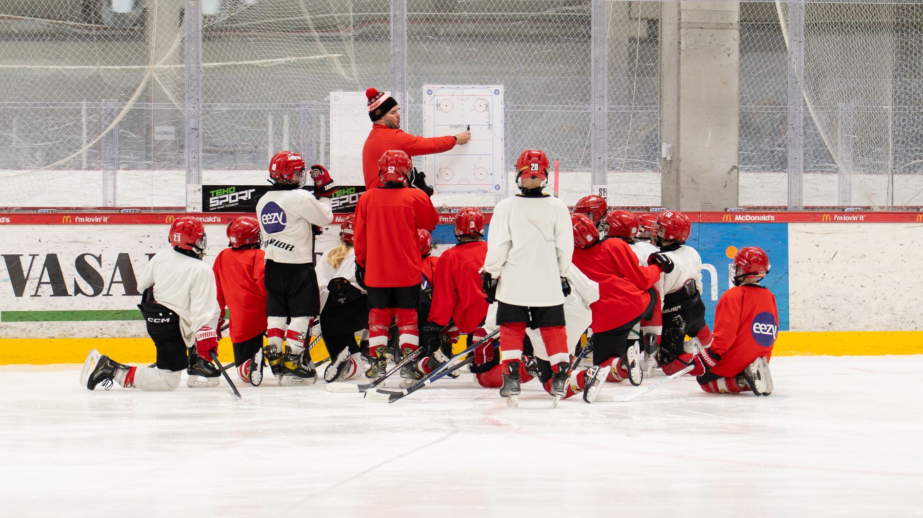 En ishockeytränare förklarar en spelstrategi för ett ungdomslag som sitter samlade på isen. 