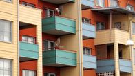 Flerfärgat bostadshus med flera balkonger, vissa utrustade med parabolantenner.