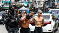 En beväpnad polis för bort två män med bar överkropp som misstänks vara gängmedlemmar i Rio de Janeiro. 