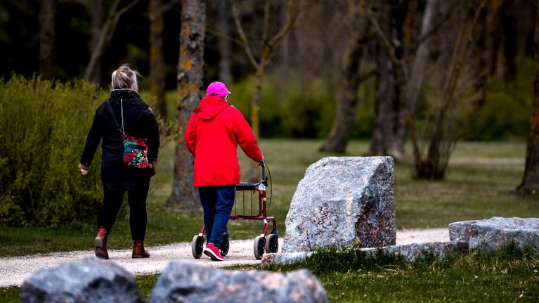 Kaksi henkilöä kävelee puistossa, toisella on rollaattori.