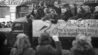 Mustavalkoinen 1940-luvun valokuva, jossa naisia tummissa takeissa heiluttaa kättään kuorma-autolle, jonka lavalla abiturientit heiluttavat.