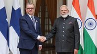 Two men in dark suits shaking hand in front of Finnish and Indian flags in the background.