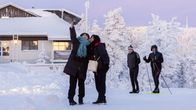 Matkailijat ottavat selfietä, hiihtäjiä nousemassa rinnettä taka-alalla. 
