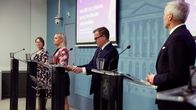Government ministers standing at speaking podiums at a press conference.