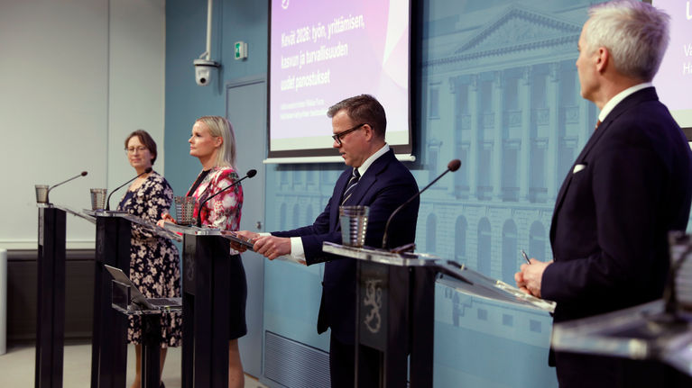 Government ministers standing at speaking podiums at a press conference.