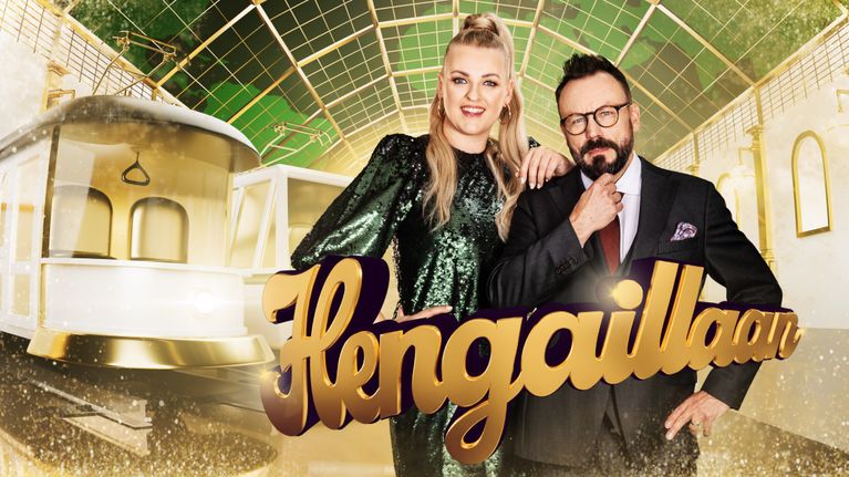 Jenni Poikelus ja Riku Rantala poseeraavat kameralle juhlavissa vaatteissa. Taustalla kullansävyinen juna-asema, etualalla Hengaillaan-teksti.