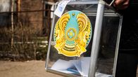 Henkilö pitää avoinna olevaa äänestyslaatikkoa, jossa on paperiääniä ja Kazakstanin vaakuna sekä teksti “Kazakhstan”.