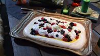 Marenkikakku kuorrutettuna lemon curdilla, kermavaahdolla sekä marjoilla tarjottimella pöydällä.