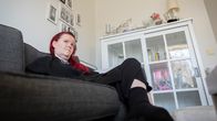 Sanna Jokinen istuu sohvalla olohuoneessaan, jossa esineitä vitriinissä ja valokuvia seinällä.