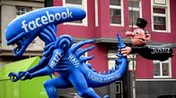 Sinisen alien patsaan hännästä pitää kiinni lennossa oleva tuomarihahmo. Alien edustaa Facebookkia ja tuomari oikeutta.