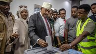 Abdirahman Mohamed Abdullahi laittaa äänestyslipuketta vaaliuurnaan. Vaalivirkailija heijastinliivissä ohjeistaa vieressä. Ympärillä joukko ihmisiä seuraa tilannetta.
